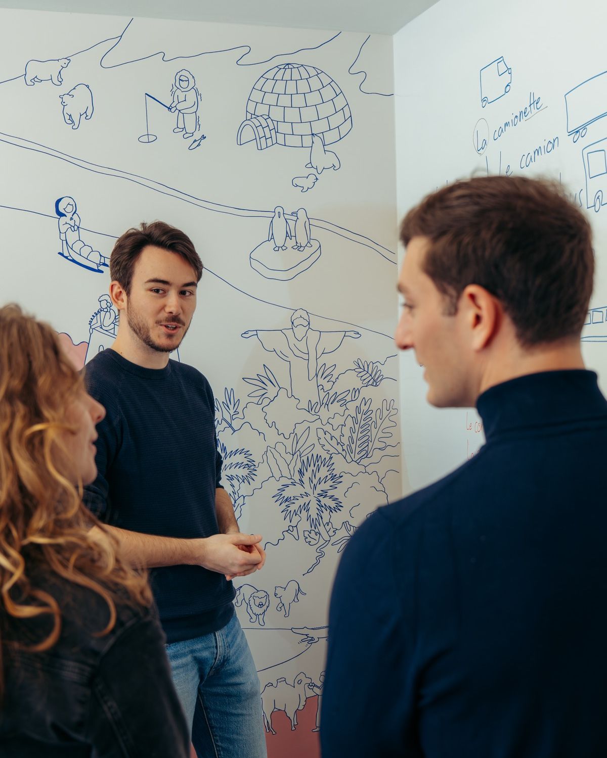 Trois personnes en conversation devant la fresque murale de l'école